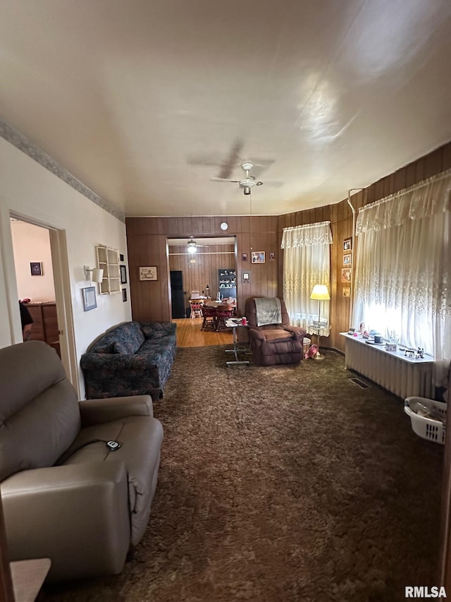 carpeted living room with wooden walls and ceiling fan