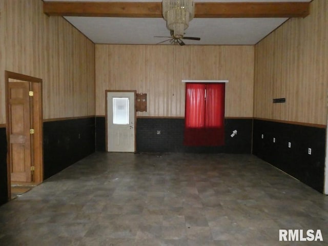 empty room featuring ceiling fan, lofted ceiling with beams, and wood walls