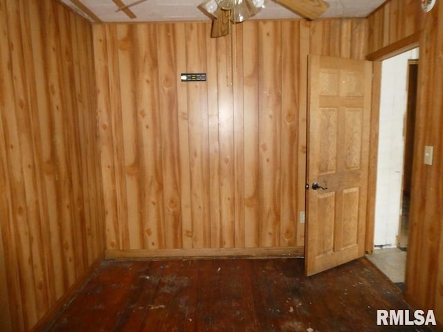 unfurnished room featuring ceiling fan, dark hardwood / wood-style floors, and wooden walls