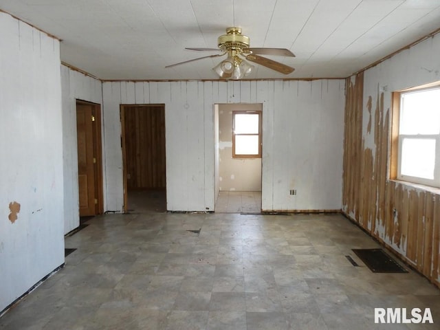 unfurnished room with ceiling fan and wood walls