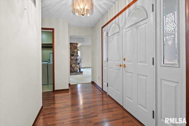 hallway with a notable chandelier, dark wood-type flooring, washing machine and clothes dryer, and a textured ceiling