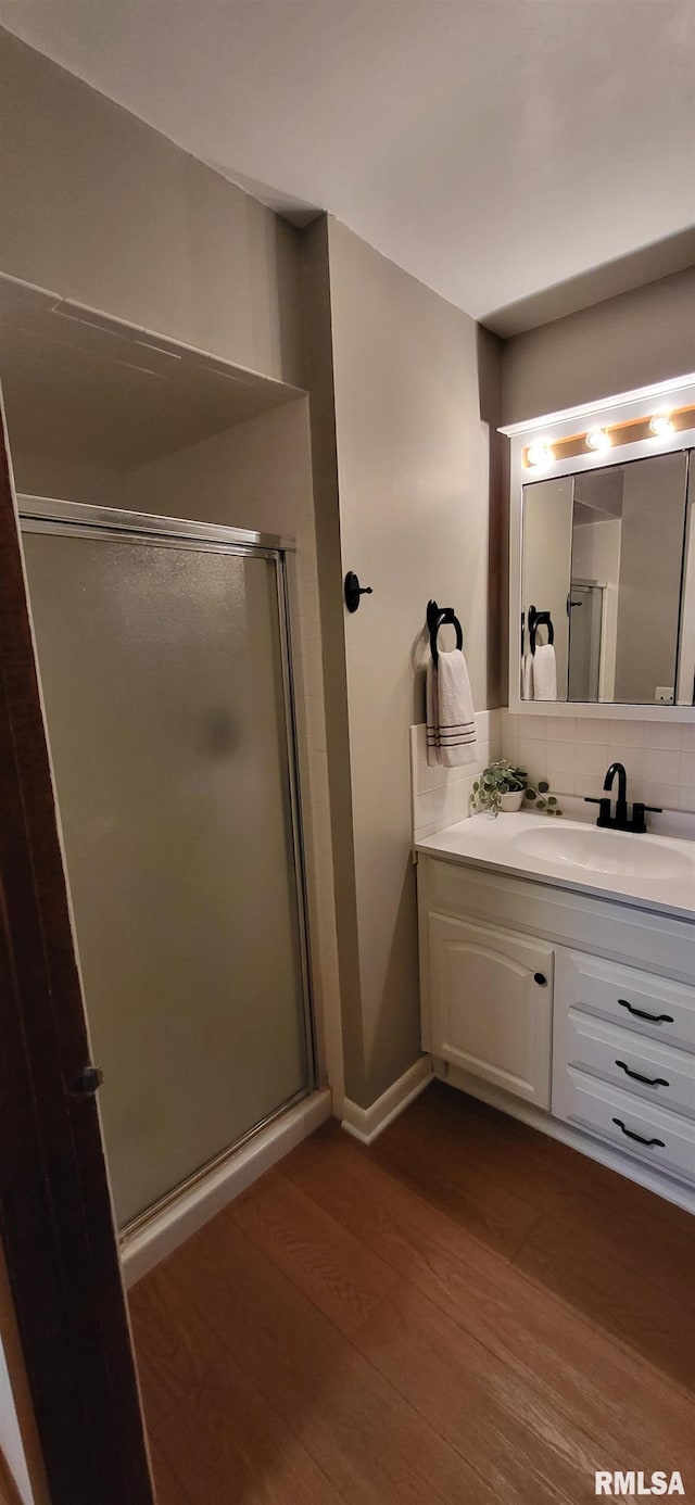 bathroom with wood-type flooring, a shower with door, vanity, and backsplash