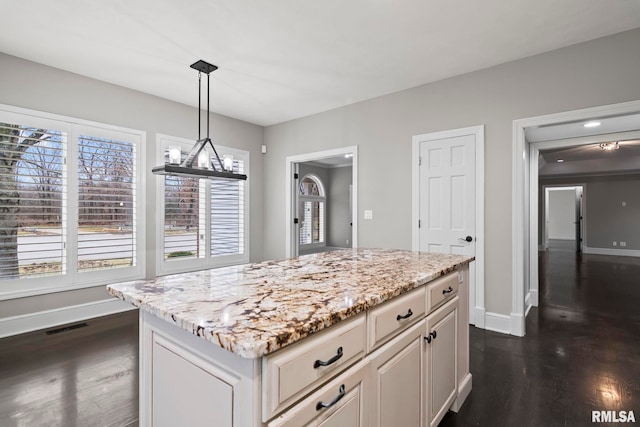 kitchen with a center island, hanging light fixtures, dark hardwood / wood-style floors, a healthy amount of sunlight, and light stone countertops