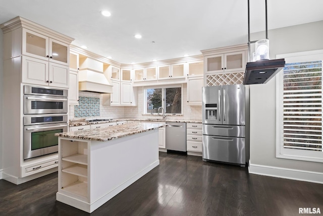 kitchen featuring premium range hood, a kitchen island, appliances with stainless steel finishes, decorative light fixtures, and light stone countertops