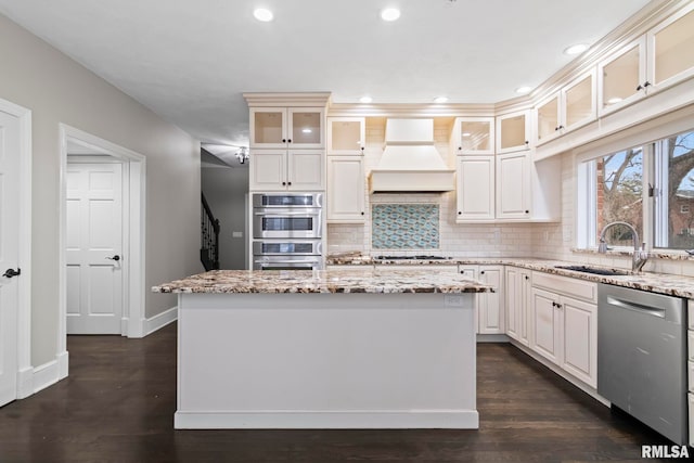 kitchen featuring appliances with stainless steel finishes, sink, a center island, light stone counters, and custom range hood