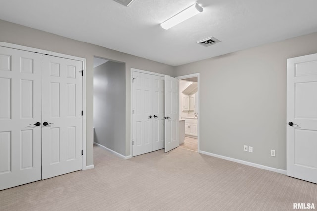 unfurnished bedroom featuring multiple closets, ensuite bathroom, and light carpet