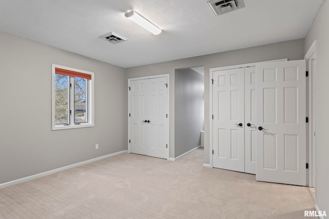 unfurnished bedroom featuring light carpet, a textured ceiling, and multiple closets