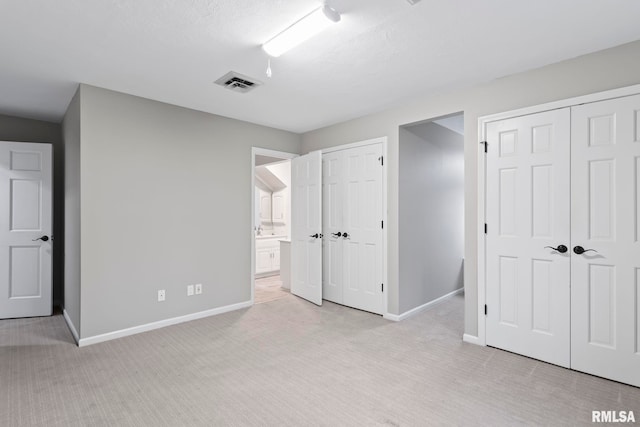 unfurnished bedroom with multiple closets, light colored carpet, a textured ceiling, and ensuite bath