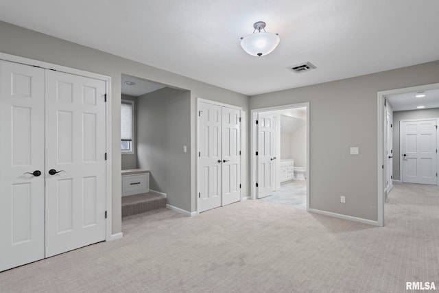 unfurnished bedroom featuring light carpet, two closets, and connected bathroom