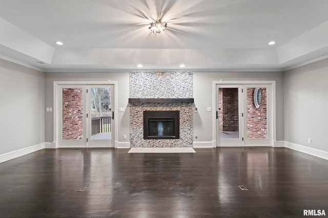 unfurnished living room featuring dark wood-type flooring, a tray ceiling, and a tile fireplace