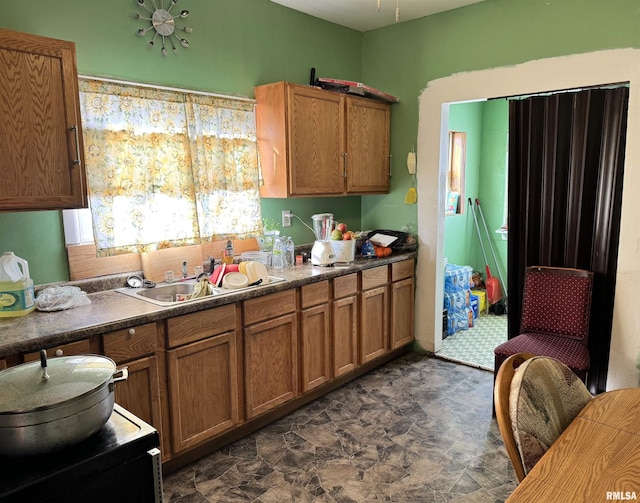 kitchen featuring brown cabinetry, dark countertops, stone finish floor, and a sink