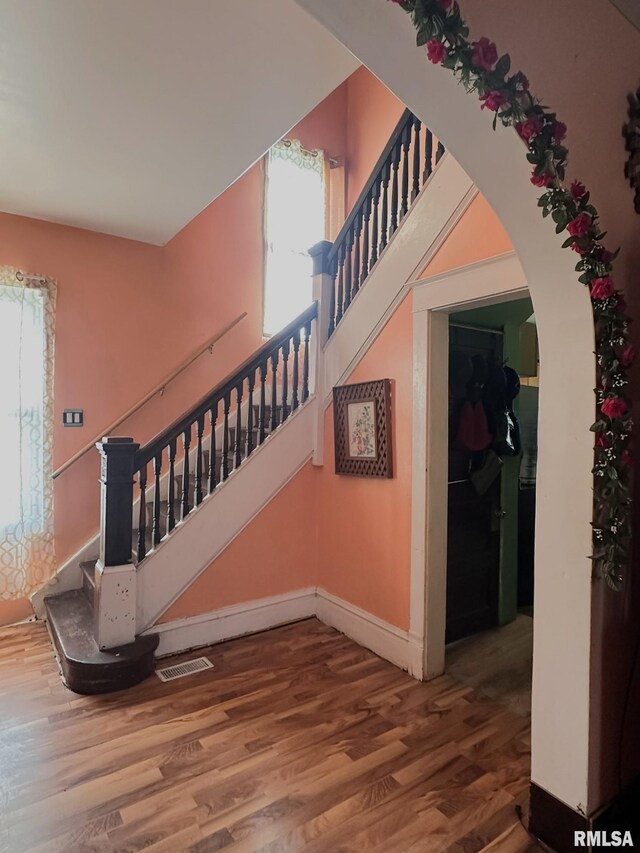 staircase with baseboards, visible vents, arched walkways, and wood finished floors