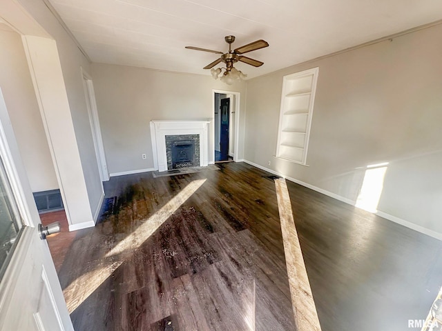 unfurnished living room with dark wood-type flooring, a fireplace with flush hearth, a ceiling fan, baseboards, and built in features