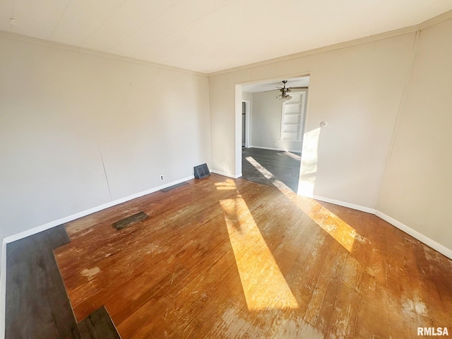 empty room with ornamental molding, hardwood / wood-style floors, a ceiling fan, and baseboards