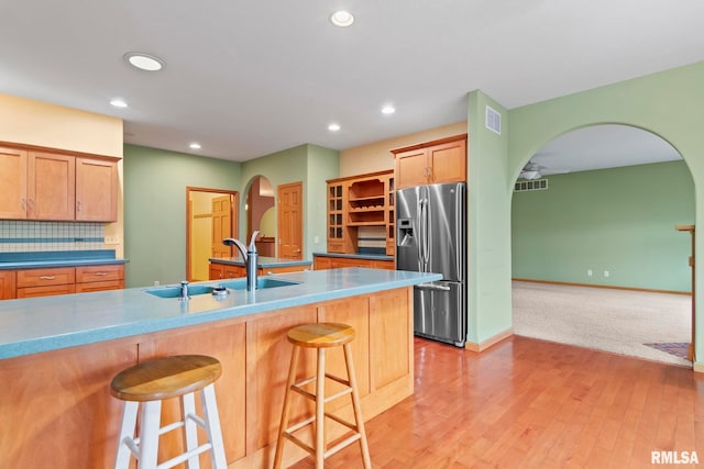 kitchen featuring a breakfast bar, sink, light wood-type flooring, stainless steel fridge, and backsplash