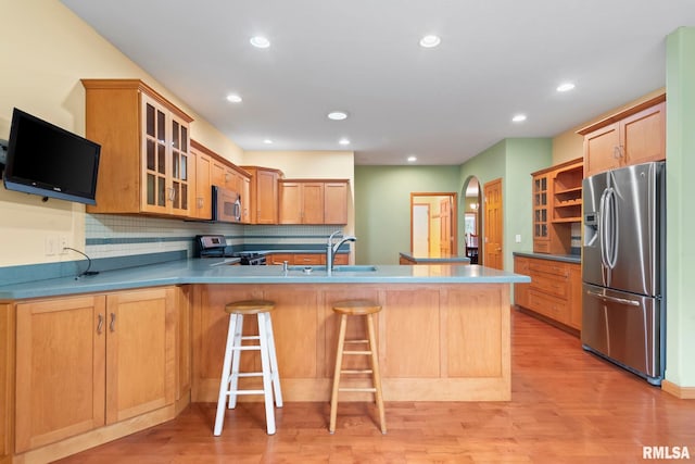 kitchen with sink, appliances with stainless steel finishes, light hardwood / wood-style floors, a kitchen bar, and kitchen peninsula