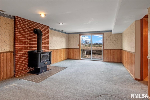 unfurnished living room with light carpet, wood walls, and a wood stove