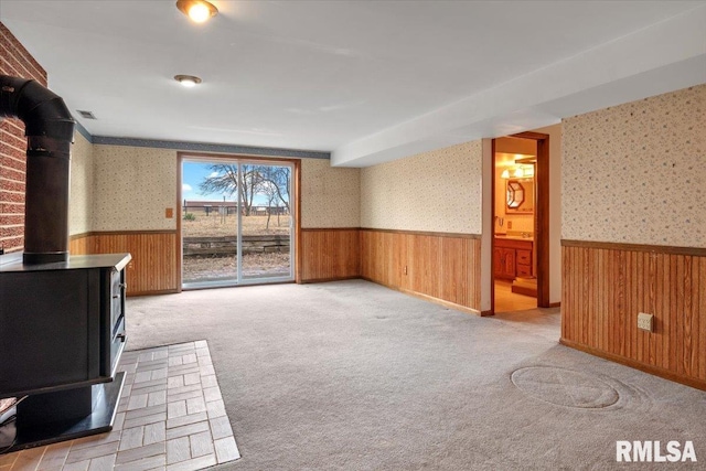 unfurnished living room featuring light colored carpet, wooden walls, and a wood stove