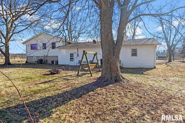 back of property with a fire pit, a lawn, and central air condition unit