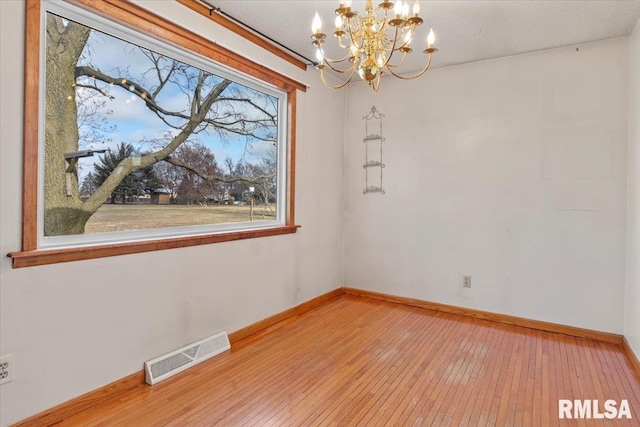 unfurnished dining area featuring light hardwood / wood-style floors, a textured ceiling, and a notable chandelier