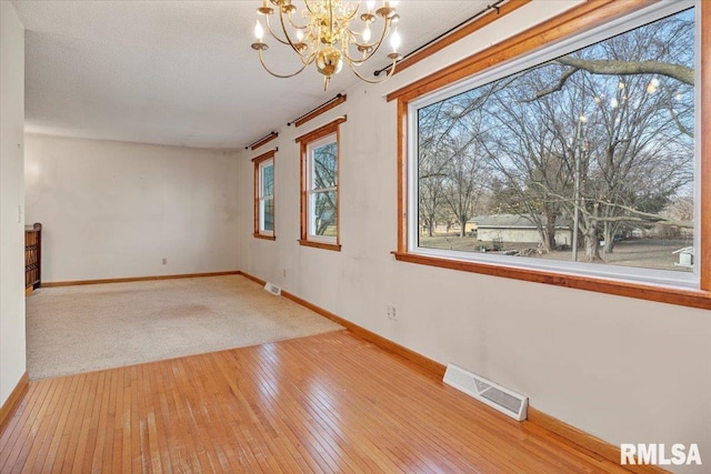 empty room featuring a textured ceiling, an inviting chandelier, and light hardwood / wood-style flooring