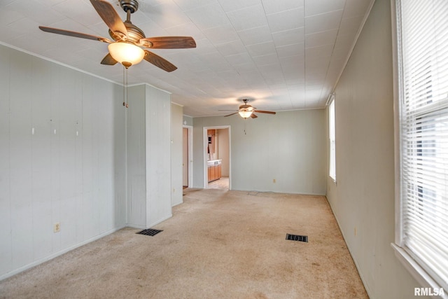 carpeted spare room featuring ornamental molding, a healthy amount of sunlight, and ceiling fan