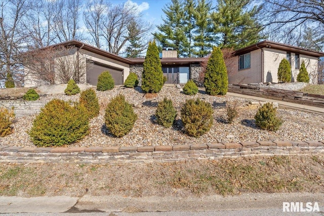 mid-century modern home featuring stone siding, an attached garage, and a chimney