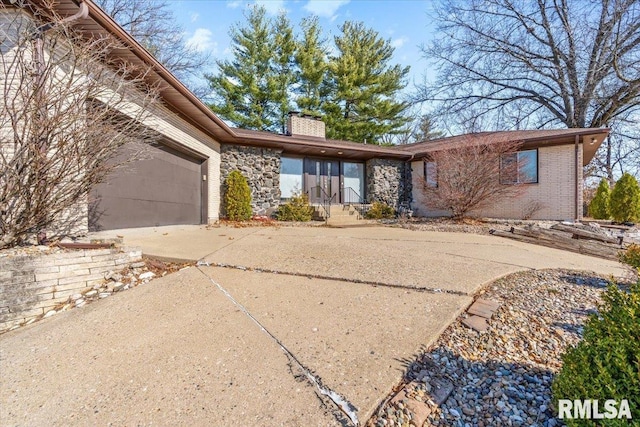 view of front of property with driveway, stone siding, a garage, brick siding, and a chimney