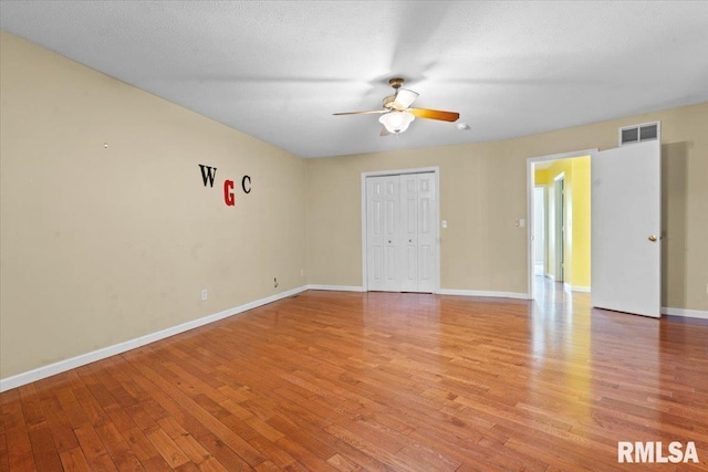 spare room featuring visible vents, baseboards, light wood-style floors, a textured ceiling, and a ceiling fan