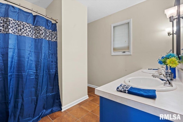 full bath with tile patterned flooring, baseboards, double vanity, a textured ceiling, and a sink