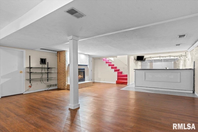 finished basement featuring visible vents, a textured ceiling, wood finished floors, a large fireplace, and stairs