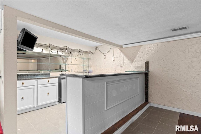 interior space featuring visible vents, light tile patterned floors, a textured wall, white cabinets, and a textured ceiling