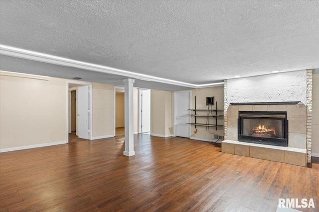 unfurnished living room with a tiled fireplace, a textured ceiling, baseboards, and wood finished floors