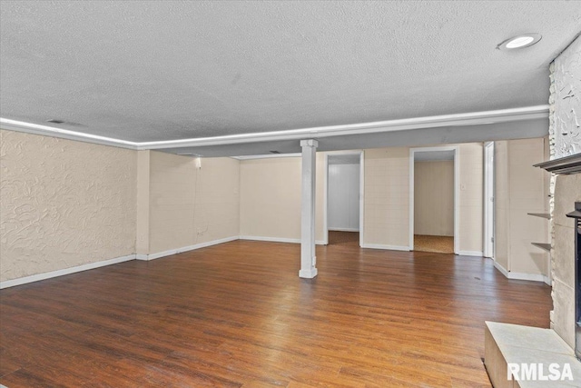 finished below grade area featuring a textured ceiling, a large fireplace, a textured wall, and wood finished floors