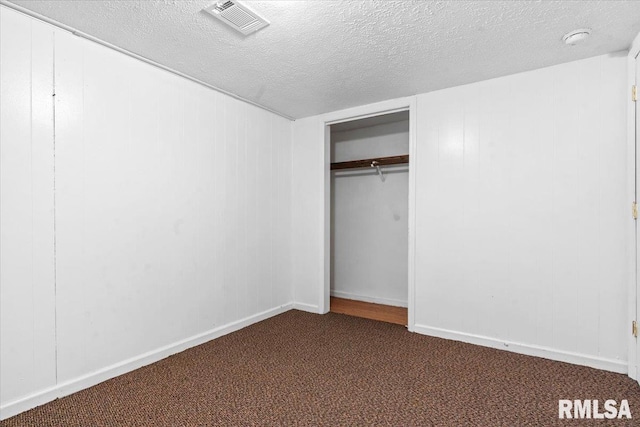 unfurnished bedroom featuring visible vents, baseboards, a closet, a textured ceiling, and dark colored carpet