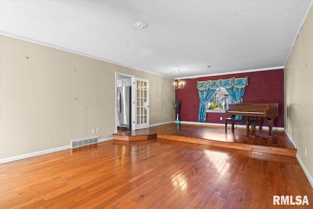 interior space featuring visible vents, baseboards, a chandelier, ornamental molding, and hardwood / wood-style flooring