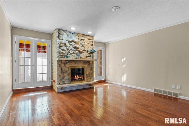 unfurnished living room featuring visible vents, hardwood / wood-style floors, a stone fireplace, french doors, and a textured ceiling