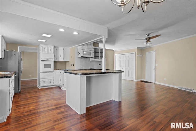 kitchen featuring ornamental molding, dark countertops, white cabinetry, white appliances, and dark wood-style flooring