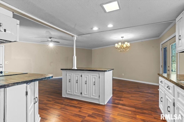 kitchen featuring dark countertops, a kitchen island, ornamental molding, ceiling fan with notable chandelier, and dark wood-style flooring