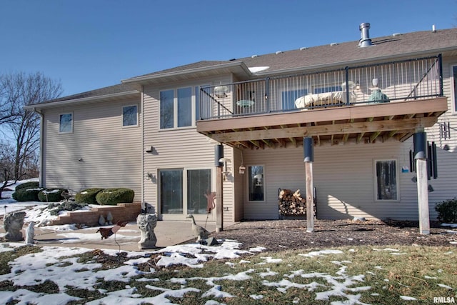 snow covered rear of property featuring a balcony and a patio