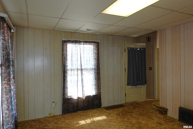 carpeted empty room with a paneled ceiling and wooden walls