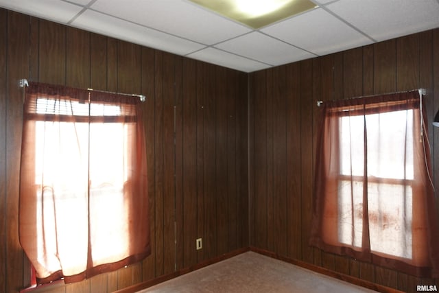 unfurnished room with a drop ceiling and wood walls