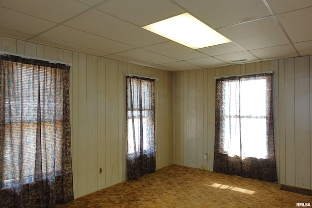 empty room with carpet floors, a paneled ceiling, and wooden walls