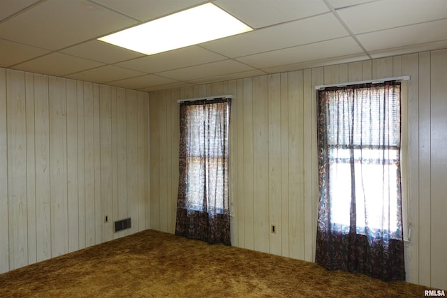 spare room featuring carpet, a paneled ceiling, and wooden walls