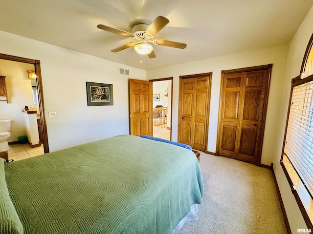 carpeted bedroom with connected bathroom, multiple closets, and ceiling fan