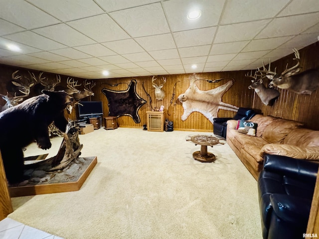 living room featuring wooden walls, carpet flooring, and a drop ceiling