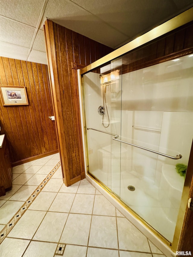 bathroom featuring a shower with door, tile patterned flooring, and wood walls