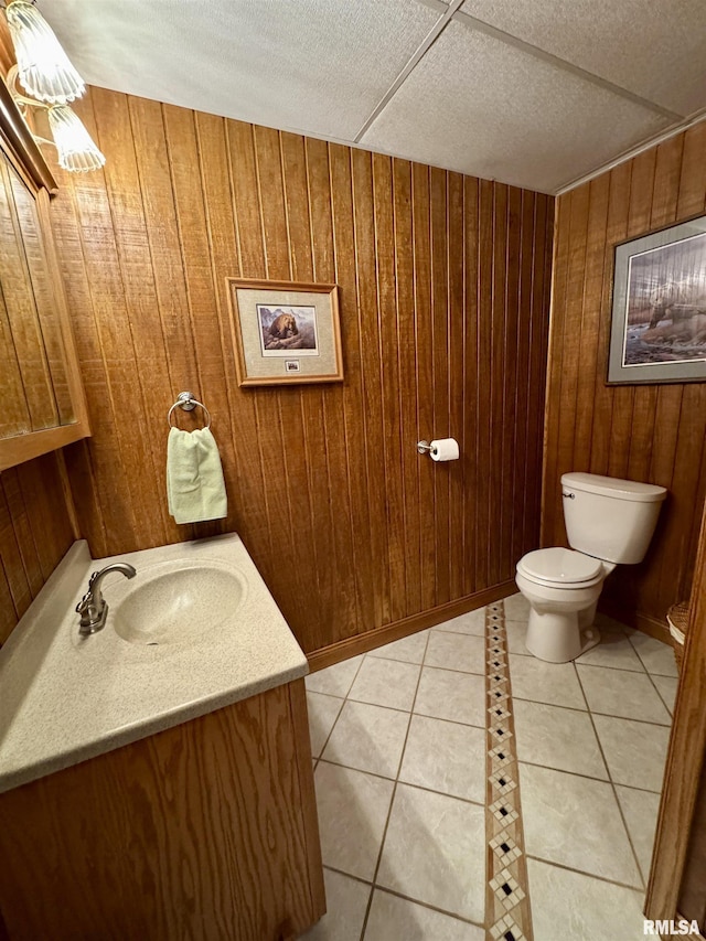 bathroom featuring tile patterned flooring, vanity, wooden walls, and toilet