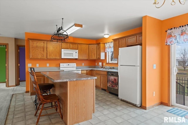 kitchen with sink, white appliances, a breakfast bar area, hanging light fixtures, and a kitchen island