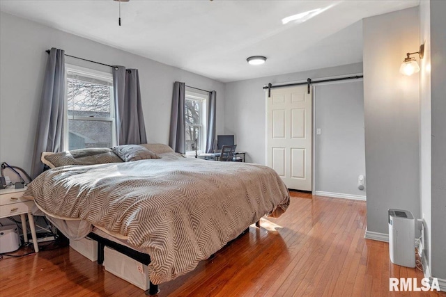 bedroom with wood-type flooring, a barn door, and multiple windows